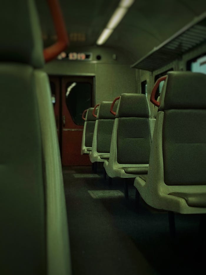 Interior view of an empty train car with rows of upholstered seats, lit dimly.
